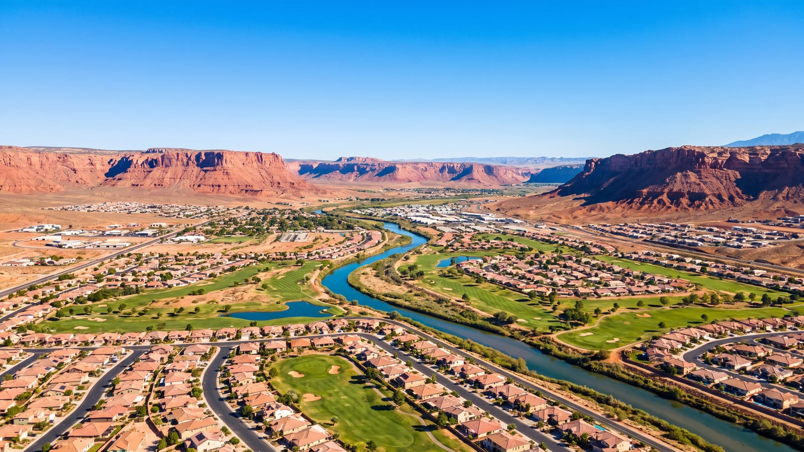 Aerial view of Mesquite Nevada with the Virgin River valley, golf courses, neighborhoods, and red mesa cliffs under blue sky